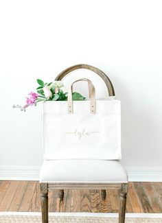 a white tote bag sitting on top of a wooden chair with flowers in it