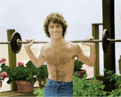 a man with no shirt lifting a barbell in front of potted plants and flowers