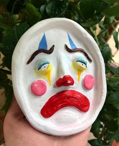 a painted face on a white plate in front of a plant