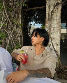 a woman sitting on the ground with a drink in her hand and tattoos on her arm