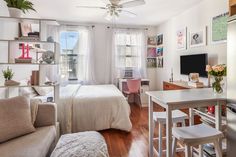 a living room with a bed, desk and television in the corner next to a window