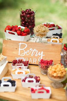 a wooden sign sitting on top of a table filled with fruit and desserts covered in white lettering