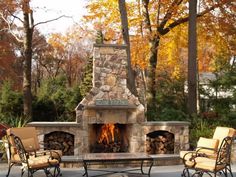 an outdoor fireplace with chairs around it and trees in the backgroung area