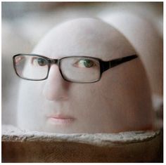 a close up of a person's head with glasses on and an egg in the background