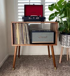 a record player sitting on top of a wooden table next to a plant and a laptop computer