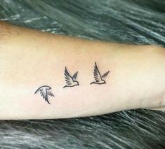 three birds flying in the air on someone's left arm, and one is black ink