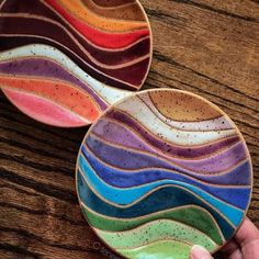 a hand holding two colorful plates on top of a wooden table