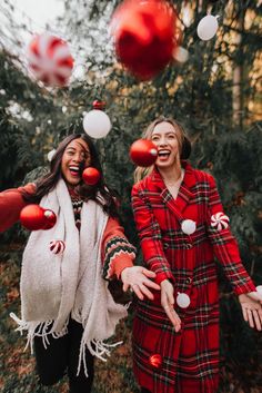 two women dressed in red and white are playing with christmas ornaments outside on the ground