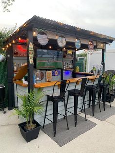 an outdoor bar with stools and lights on the roof, next to potted plants