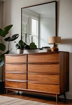 a wooden dresser sitting in front of a mirror next to a potted plant on top of a rug