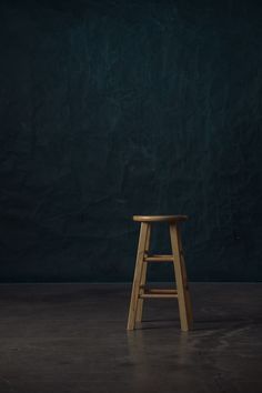 a wooden stool sitting on top of a cement floor next to a dark green wall