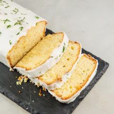 a loaf of cake with white frosting and sprinkles on it sitting on a slate platter