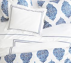 a bed with blue and white sheets and pillows on top of eachother's headboard