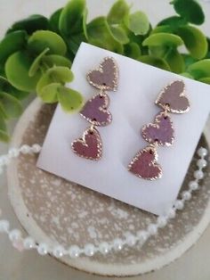 two heart shaped earrings sitting on top of a white plate next to a plant with green leaves