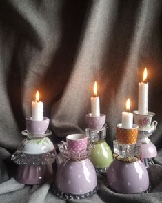 four tea cups with candles in them sitting on a cloth covered table next to each other