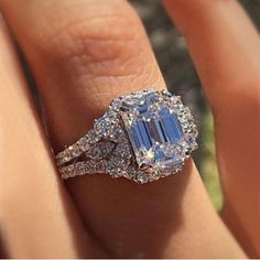 a woman's engagement ring with an emerald and diamond center stone on her finger