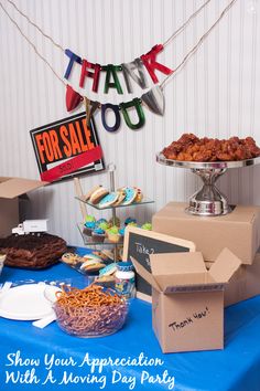 a blue table topped with lots of desserts and pastries next to a thank you for sale sign