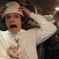 a young man in a car with his mouth open and wearing a funny t - shirt