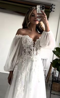 a woman taking a selfie wearing a white dress with sheer sleeves and an off the shoulder top