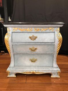 a blue and gold painted chest of drawers on a wooden floor in front of a black backdrop