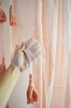 a person is holding up a curtain with tassels