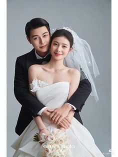 a bride and groom pose for a wedding photo shoot in front of a gray background