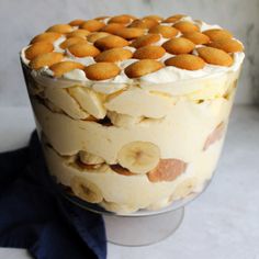 a dessert with bananas and cream in a glass dish on a white tablecloth next to a blue towel