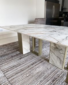 a marble dining table with metal legs in a living room or office area, next to a refrigerator