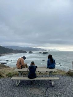 two people sitting at a picnic table with the ocean in the background