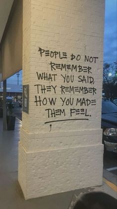 graffiti written on the side of a white brick building in front of a parking lot