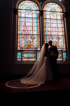 a bride and groom standing in front of a stained glass window at the end of their wedding day