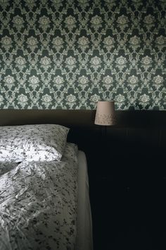 an unmade bed in front of a wallpapered headboard