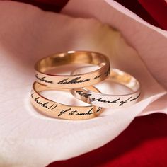 two gold wedding rings with handwriting on them sitting in front of a rose petals flower