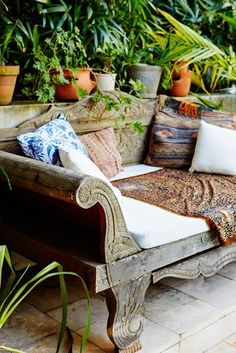 a wooden bench with pillows on top of it and potted plants in the background