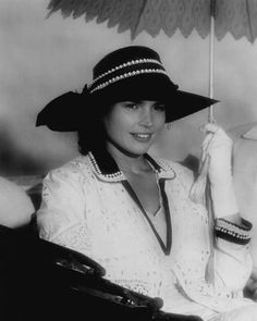 a black and white photo of a woman in a hat holding an umbrella over her head