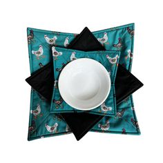 a white bowl sitting on top of a blue place mat with black napkins around it