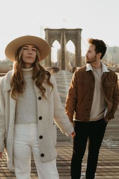 a man and woman holding hands while standing next to each other in front of the brooklyn bridge