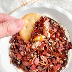 someone is dipping some kind of cracker into a bowl filled with bacon and other toppings