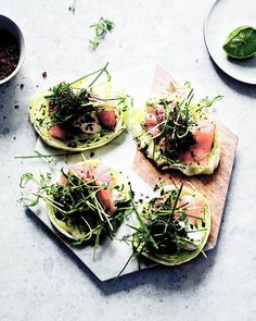 four open sandwiches with meat and greens on a cutting board