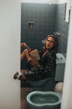 a woman sitting on the toilet reading a book