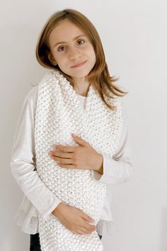 a woman wearing a white knitted shawl standing in front of a wall with her hands on her stomach