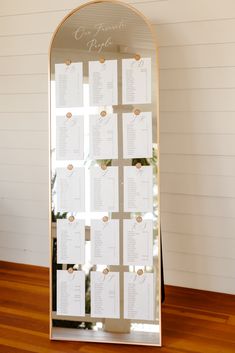 a mirror with seating cards attached to it on top of a wooden floor next to a christmas tree