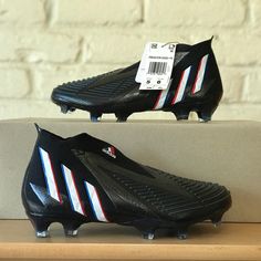 a pair of black soccer shoes with white and blue stripes on the soles sitting on a shelf