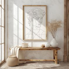 a white vase sitting on top of a wooden table in front of a framed drawing