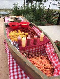 a wooden boat filled with lots of food on top of a checkered table cloth