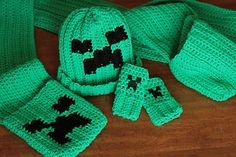 a green knitted hat, scarf and mittens on a wooden floor with the same pattern