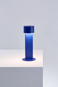 a tall blue vase sitting on top of a white table next to a gray wall