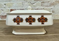 a white dish with three orange designs on the front and bottom, sitting on a wooden table