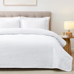 a bed with white comforter and pillows in a hotel room or apartment setting,