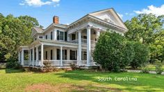 a large white house sitting in the middle of a lush green field next to trees